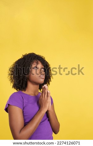 Afro woman praying while looking up joining hands