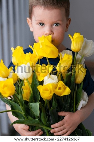 A little boy holds a large bouquet of yellow and white tulips. A portrait of a child with a bouquet of flowers, a gift, a surprise, mother's day, March 8, birthday. A gift for friends and relatives