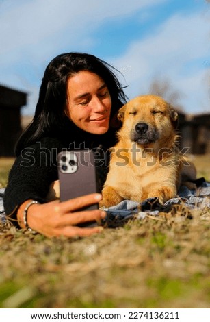 a beautiful brunette in a black sweater, lies on the grass with a homeless dog, the girl hugs the dog, takes pictures with him and takes care of him, a beautiful red dog