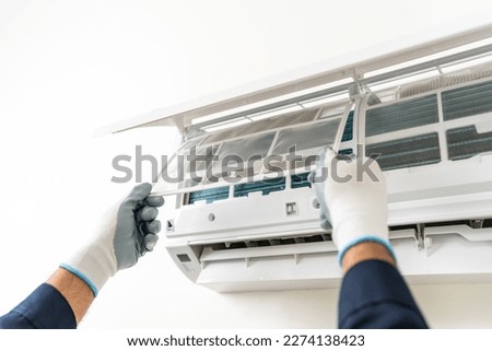 Air conditioner service indoors. Air conditioner cleaning technician He opened the front cover and took out the filters and washed it. He in uniform wearing rubber Royalty-Free Stock Photo #2274138423
