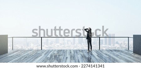 Back view of young businesswoman looking into the distance on rooftop with bright daylight sky and wide city view. Success, future and vision concept Royalty-Free Stock Photo #2274141341