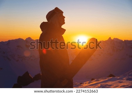 silhouette of a skier with skis standing on a slope at sunset against a mountain range. sportsman portrait