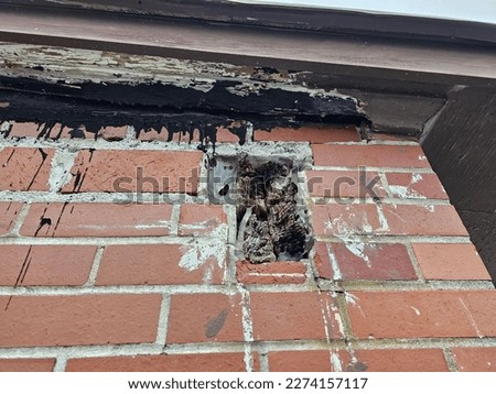 A hole in the side of a brick building with wood still there from the broken overhang.