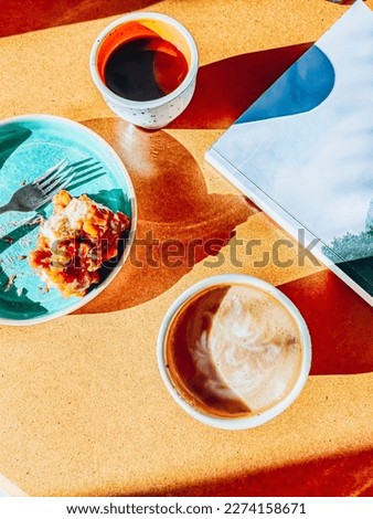 Americano and cappuccino, cheesecake and magazine on yellow table in Cafe. Sunny day. Flat lay. Top view