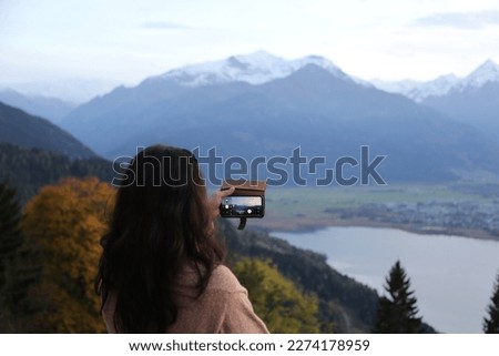 Woman taking a picture of Alps with smartphone at dusk