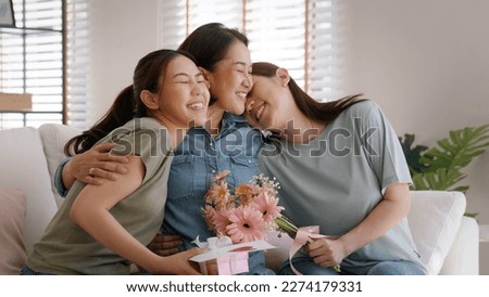 Mother day two grown up child cuddle hug give flower gift box red heart card to mature mum. Love kiss care mom asia middle age adult three people sitting at home sofa happy smile enjoy family time.