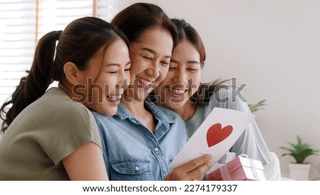Mother day two grown up child cuddle hug give flower gift box red heart card to mature mum. Love kiss care mom asia middle age adult three people sitting at home sofa happy smile enjoy family time. Royalty-Free Stock Photo #2274179337