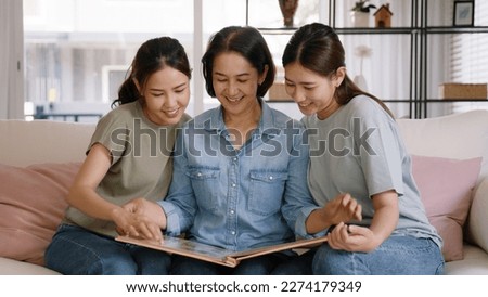 Recall the past life memories Happy time Mother's day grown up kid child joy fun look at old retro photo album with mature mum. Asia adult people middle age mom smile enjoy relax sitting at home sofa.