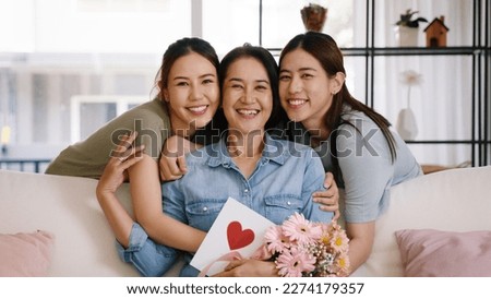 Happy time Mother day grown up child looking at camera cuddle hug give flower gift box red heart card to mature mum. Love kiss care mom asia middle age adult people smile enjoy sitting at home sofa. Royalty-Free Stock Photo #2274179357
