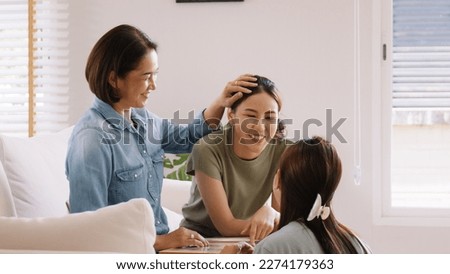 Middle aged mom smile look at two grown up kid child relax hug cuddle stroking with love care warm time. Asia people woman adult older mum parent sitting at home sofa sweet trust moment happy life. Royalty-Free Stock Photo #2274179363