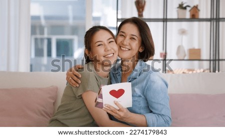 Happy time Mother day grown up child girl looking at camera cuddle hug give gift box heart card to mature mum. Love kiss care mom asia middle age adult people smile enjoy relax sitting at home sofa.