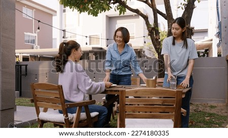 Group of man woman asia people fun joy prepare set dine table plate glass cutlery in cozy party host event at home front yard patio. Young adult child friend enjoy happy warm time picnic lunch meal.