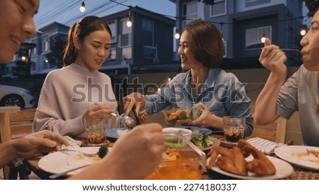 Mom enjoy thai meal cooking for family day home dining at dine table cozy patio. Mum passing serving food to group four asia people young adult man woman friend fun joy relax warm night picnic eating.