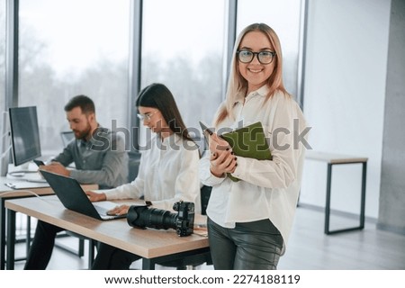 Woman in glasses is standing with notepad in hands. Successful team are working together in the office.