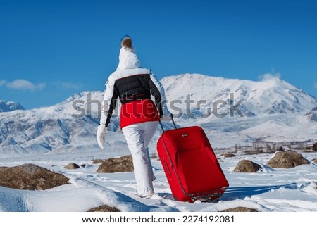 Young woman traveling with red suitcase on winter mountains background