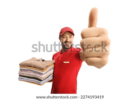 Laundry worker holding a pile of clothes and gesturing thumbs up isolated on white background