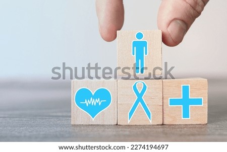 Person placing block with icon of man on cubes with painted plus and heart against symbol of prostate cancer awareness