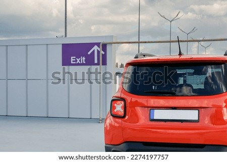 A red car stands in front of the exit of the parking lot