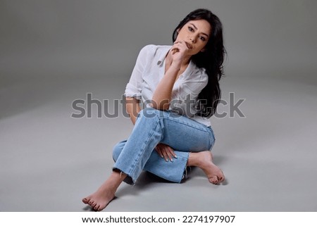 Portrait of beautiful brunette woman in casual clothes posing in studio on gray background.