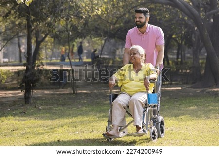 Son walking with disabled mother in wheelchair at park