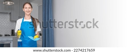 Young smiling woman in a uniform apron holds a bottle of detergent and a napkin. Hiring a qualified home care agency, a quick and simple housekeeping concept. Cleaning company. House cleaning. Banner