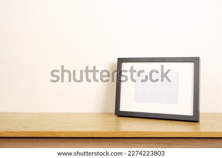 Horizontal empty black photo frame on wooden side table. Blank wall with copy space.