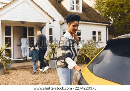 Woman charging electric car on driveway outside house Royalty-Free Stock Photo #2274229375