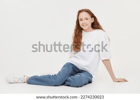 Full-length portrait of a beautiful teenage girl with long wavy hair in a white blouse and blue jeans smiling at the camera. White studio background.