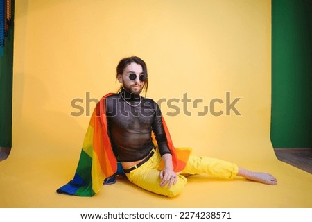 gay man with a gay pride flag smiling and looking away on yellow background.