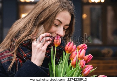 Happy stylish woman with bouquet of pink tulips talking on the phone, spring lifestyle portrait.