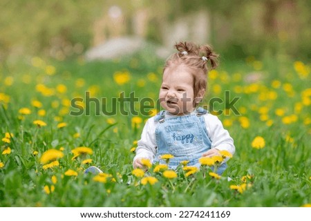 Happy little baby girl sitting on a green meadow with yellow flowers dandelions on the nature in the park
