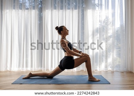 Young woman doing yoga vinyasa flow against big window with white curtains in the morning. Royalty-Free Stock Photo #2274242843