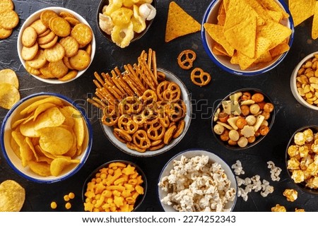 Salty snacks, party mix. An assortment of crispy appetizers, overhead flat lay shot on a black background. Potato and tortilla chips, crackers, popcorn etc Royalty-Free Stock Photo #2274252343