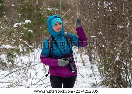 A beautiful, attractive woman in her mature years is hiking in the forest on a winter's day and taking pictures. A woman around 40-45 years old wears travel clothes and collects materials for ladart.