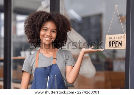 Small business african woman is a waitress in an apron, the owner of the cafe stands at the door with a sign Open waiting for customers. Small business concept, cafes and restaurants