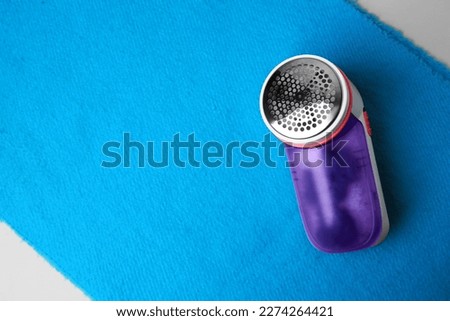 Modern fabric shaver on light blue cloth with lint, top view. Space for text