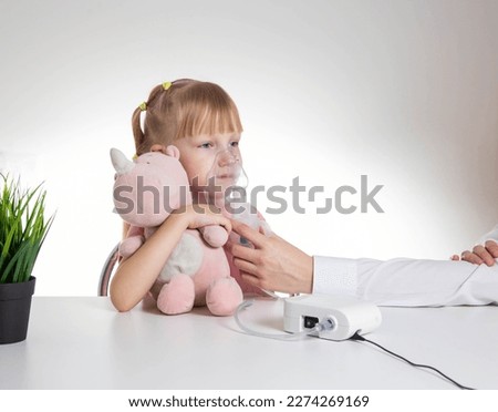 Beautiful little girl breathing into an inhaler for asthma and pneumonia at home. Treatment of diseases of the upper respiratory tract in children. Copy space for text, laryngitis Royalty-Free Stock Photo #2274269169
