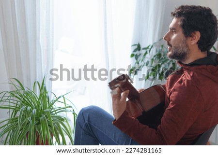 man playing Spanish guitar next to the window