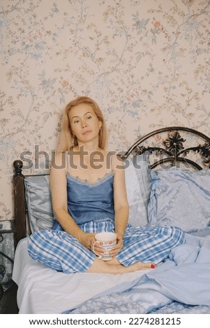 Middle aged woman sitting in bedroom enjoys morning, drinking coffee