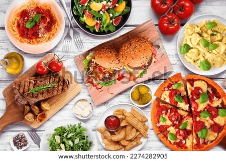 Table scene with a variety of delicious foods. Above view over a white wood background.