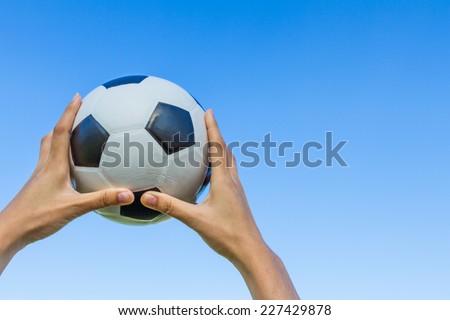 Girl hand holds a soccer ball in the sky on blue sky background.
