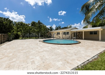 Beautiful patio of a contemporary style house, located in Miami, with lots of greenery around it, circular pool, covered patio, trees, palm trees, flower beds with plants, short grass, cement floor an