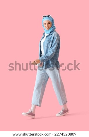 Stylish Muslim woman in blue hijab walking on pink background Royalty-Free Stock Photo #2274320809