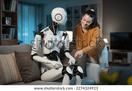A pretty young girl orders her A.I.-equipped Domestic Robot to book her a flight. Concept of usefulness and versatility of A.I.  Royalty-Free Stock Photo #2274324923