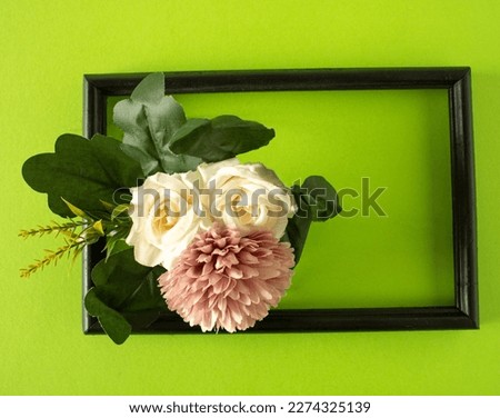 A black frame with a spring picture of two white roses and one p