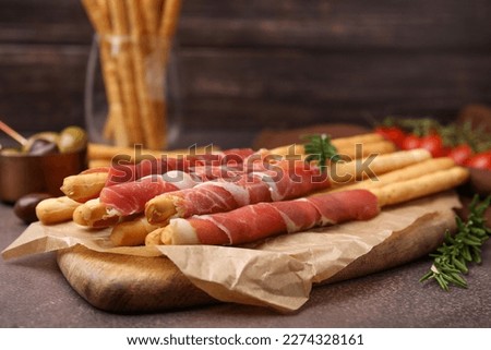 Delicious grissini sticks with prosciutto and ingredients on brown textured table Royalty-Free Stock Photo #2274328161