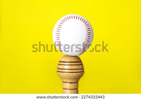 White ball on wooden baseball bat against yellow background, closeup. Sports equipment