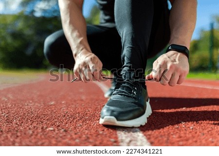 Close-up photo of a man's hand tying shoelaces at a sports stadium, a runner before starting a run and training, on a sunny day. Royalty-Free Stock Photo #2274341221