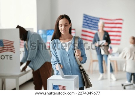 Young brunette woman in casualwear putting ballot paper into box with American flag while voting during presidential election Royalty-Free Stock Photo #2274349677