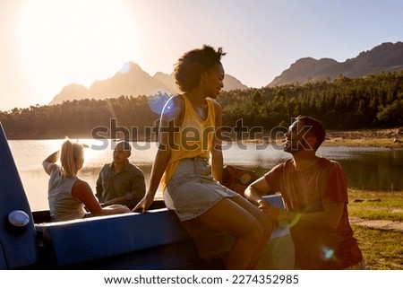 Group Of Friends With Backpacks In Pick Up Truck On Road Trip By Lake At Sunset Royalty-Free Stock Photo #2274352985